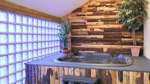 A spa area with a wooden wall, a hot tub, and a potted plant. - Cob Barn (Exeter)