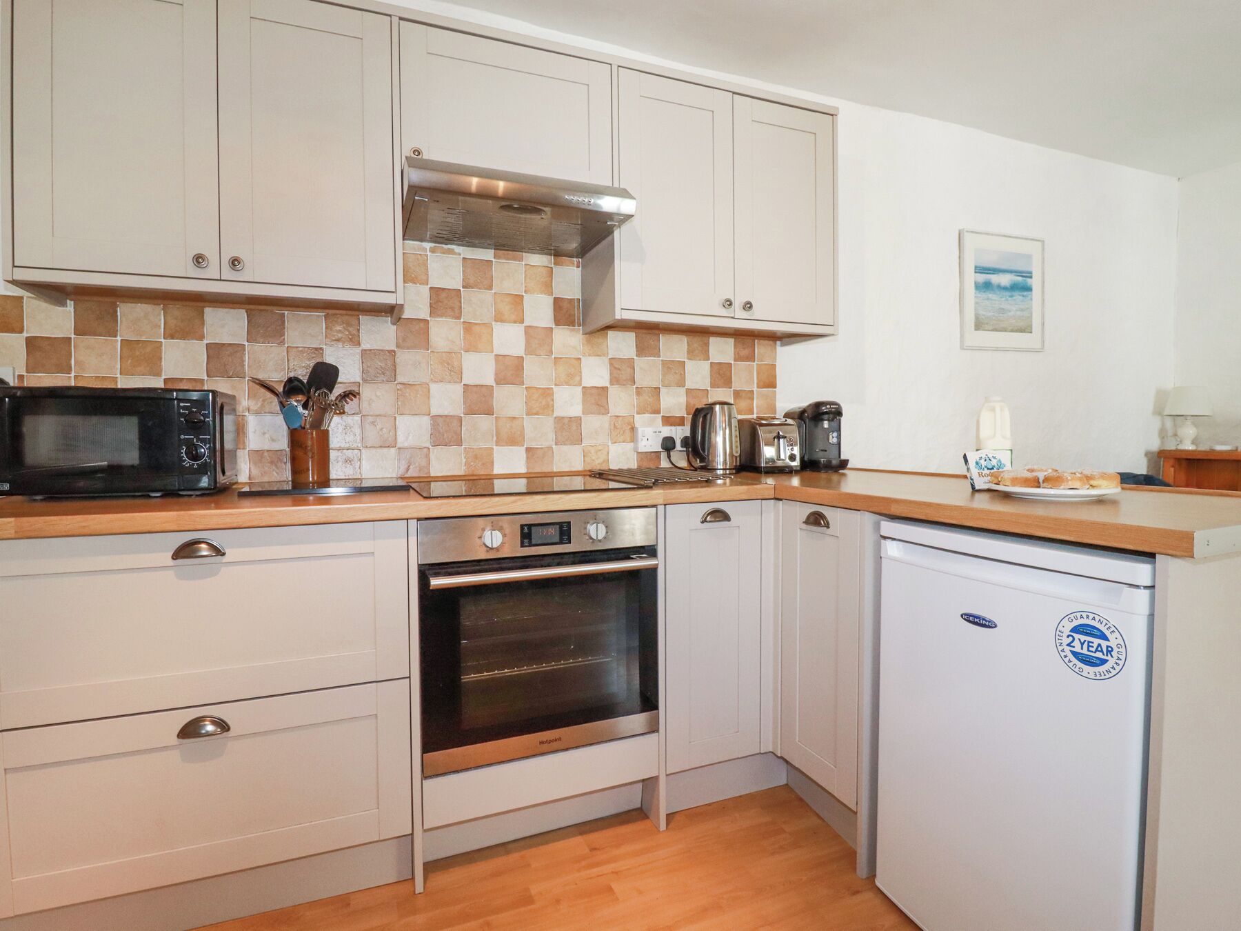 A compact kitchen with white cabinets, a microwave, a toaster, a kettle, and a dishwasher.