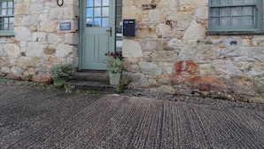 Un edificio in pietra con una porta verde, due finestre e un piccolo portico con piante in vaso.