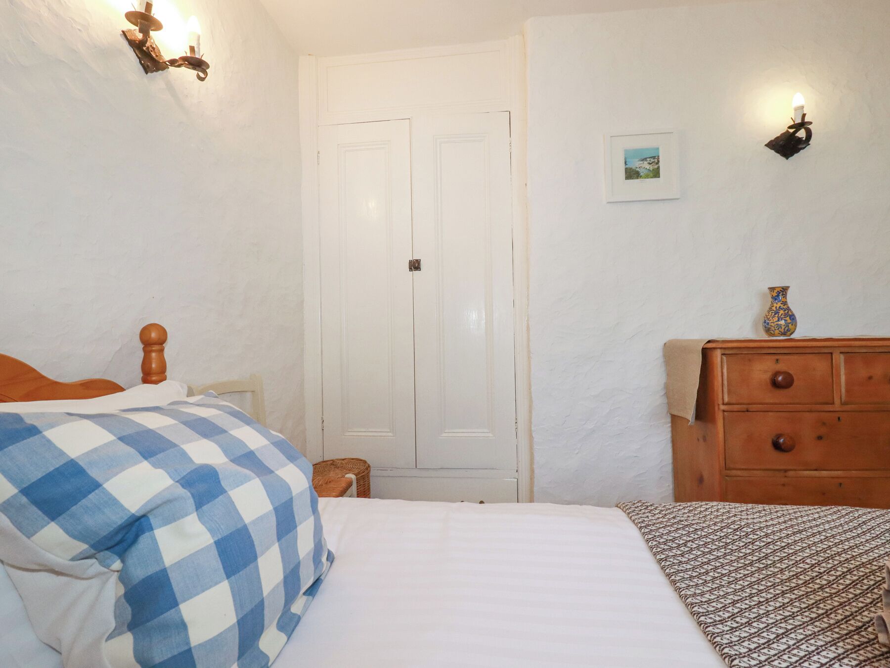 Un dormitorio con cama, cómoda, lámpara de pared y una puerta.