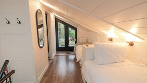 A hotel room with a wooden floor, a bed with white bedding, a small table, a chair, a mirror, and a door leading to an outdoor area. - The Blacksmith's Shop (Saltburn-by-the-Sea)