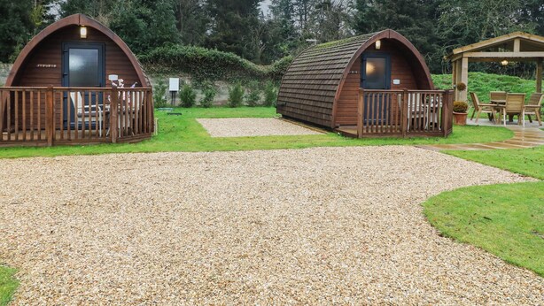 Two wooden cabins with a gravel path leading to them, surrounded by greenery. - Charlottes (Spalding)