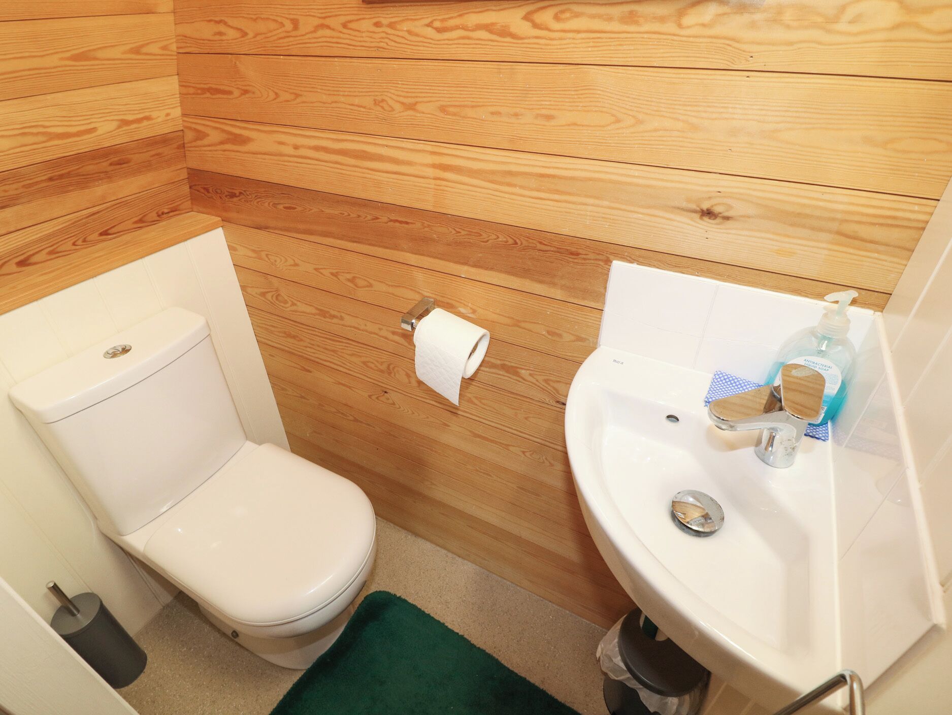 A small bathroom with a toilet, a sink, and a wooden wall.
