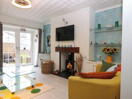 Una sala de estar con chimenea, televisor montado en la pared, mesa de centro de vidrio y sofá amarillo.
