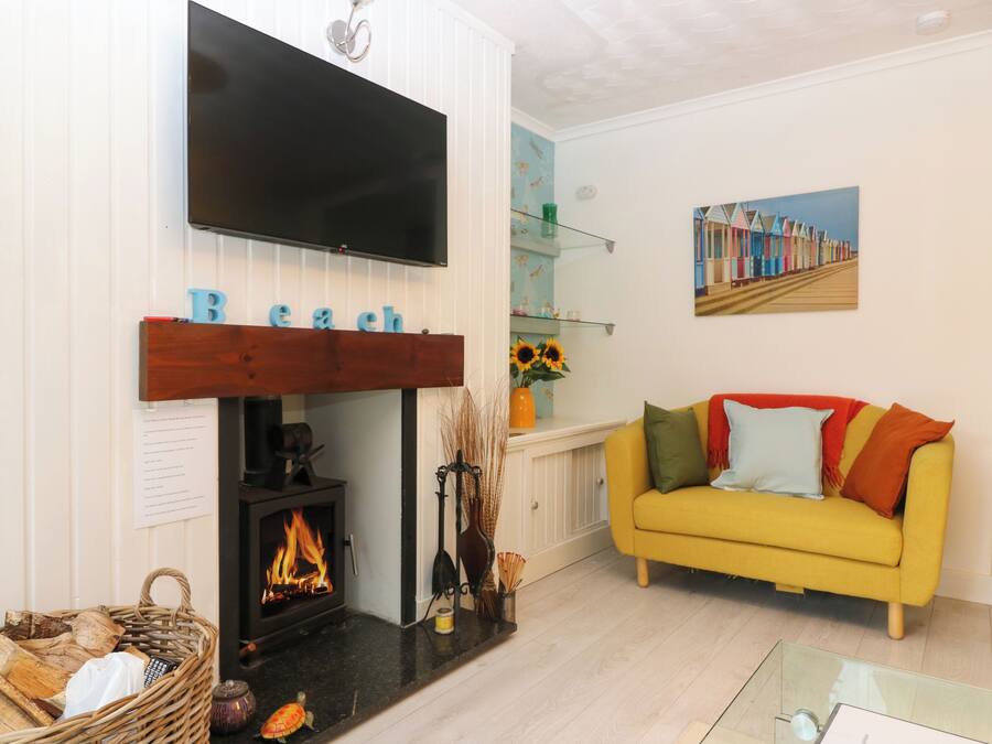 Una sala de estar con chimenea, un sofá amarillo, una estantería y un televisor de pantalla plana montado en la pared.