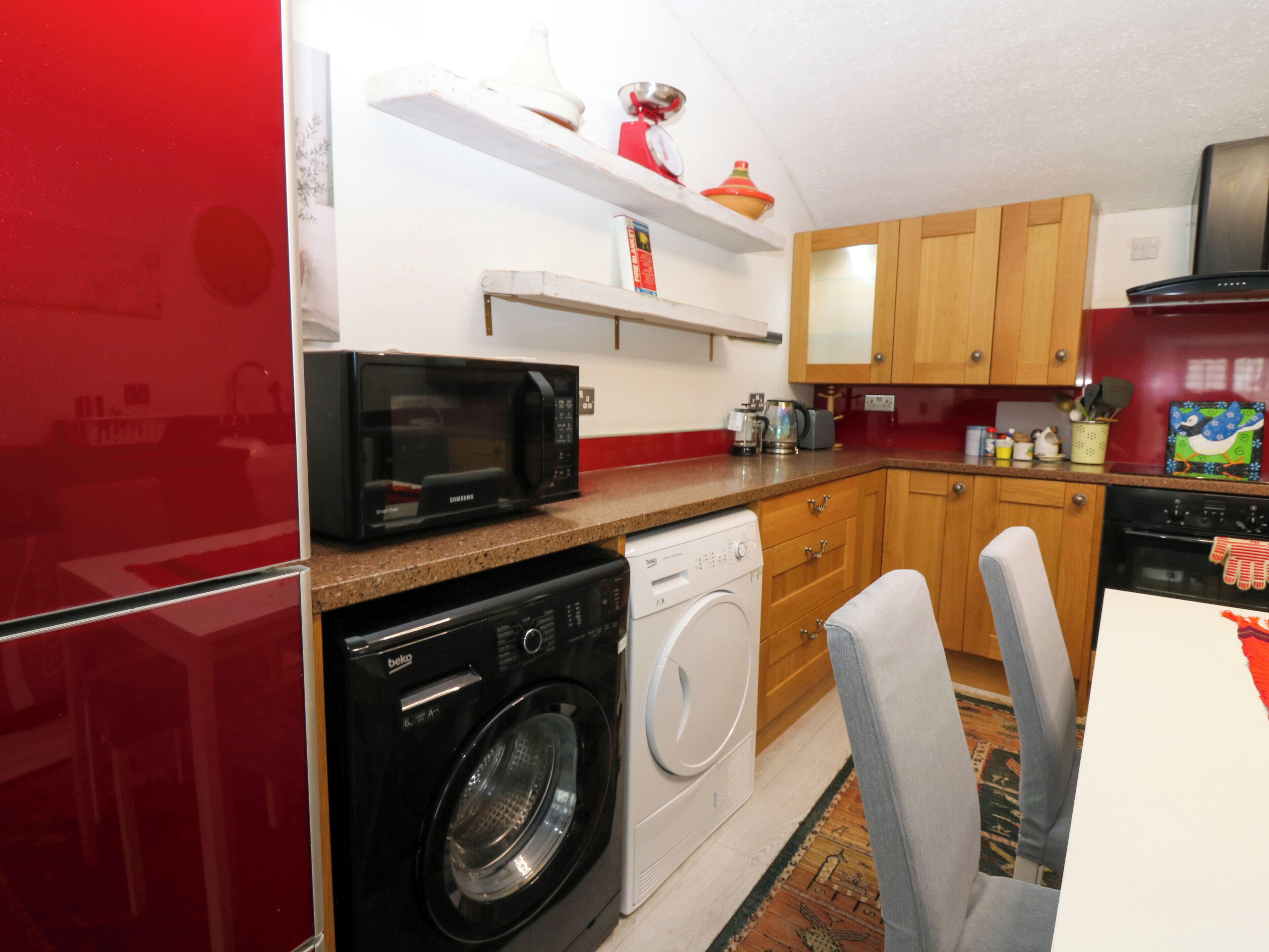 A compact kitchen with a microwave, washing machine, and wooden cabinets.