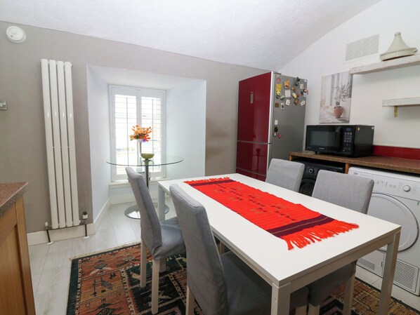 Una cocina compacta con comedor, un refrigerador rojo, un microondas y una lavadora.