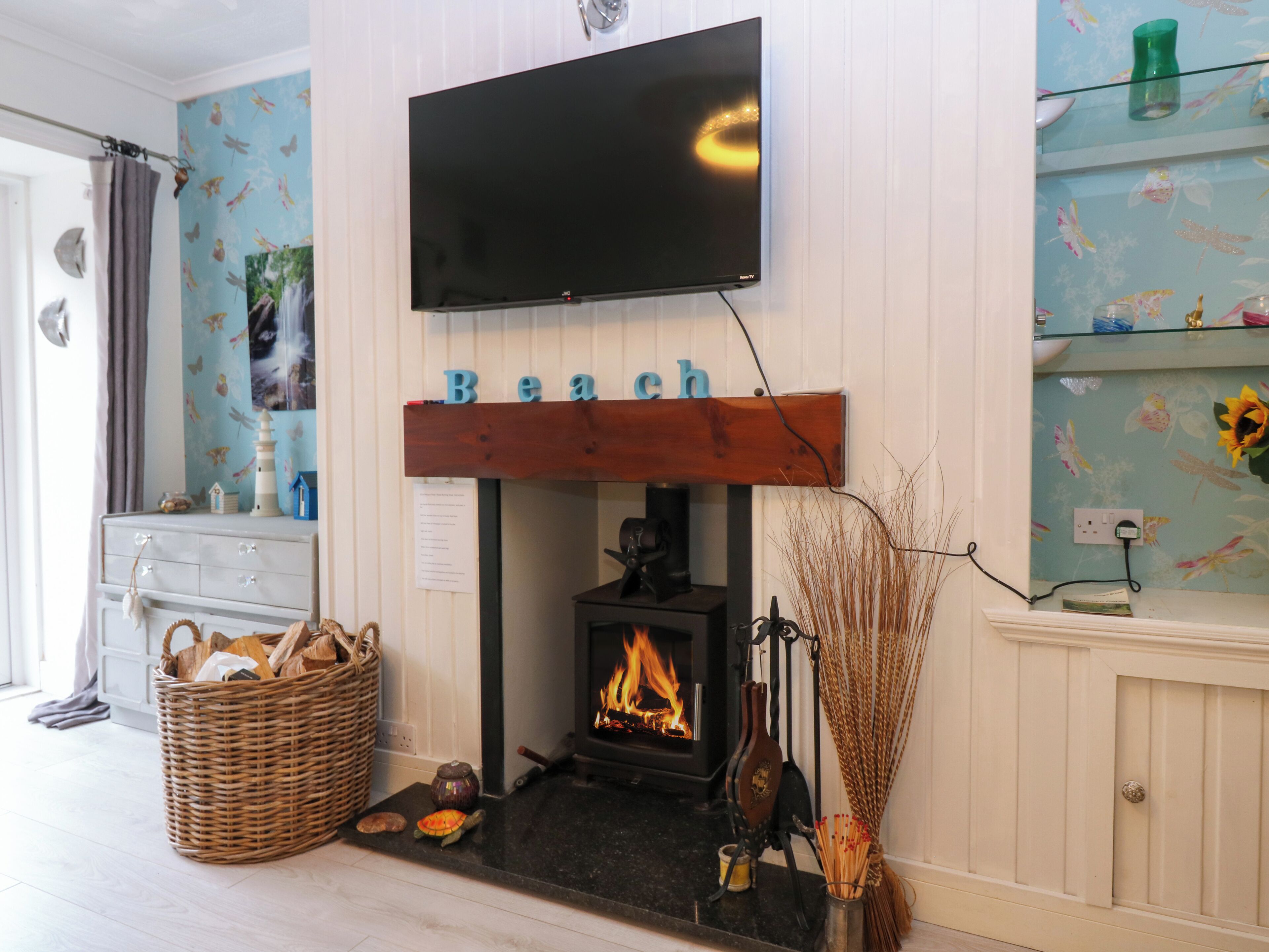 A living room with a fireplace, a television mounted above it, and a shelf with decorative items.
