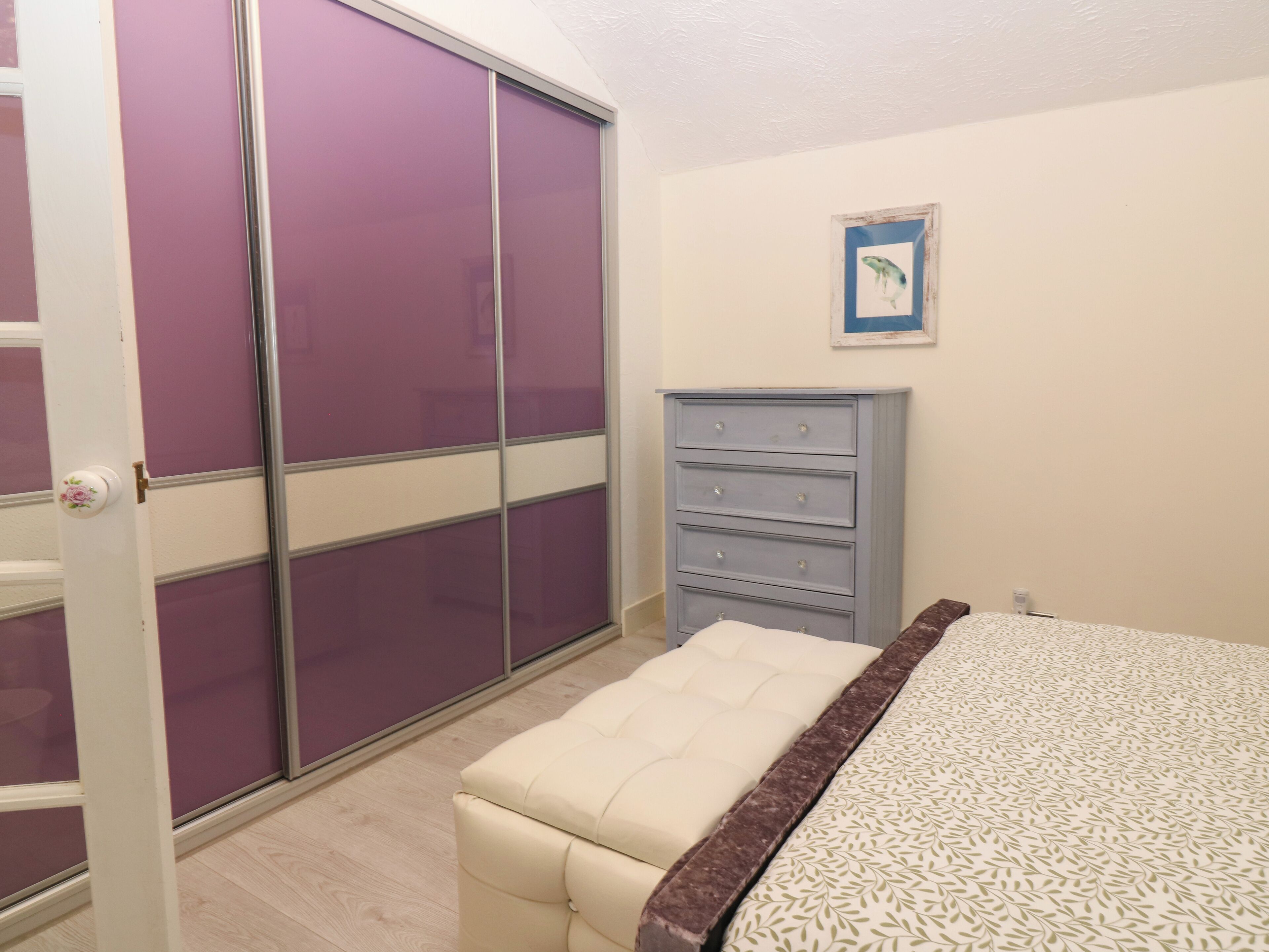 A bedroom with a bed, a dresser, a bench, a wardrobe, and a framed picture on the wall.