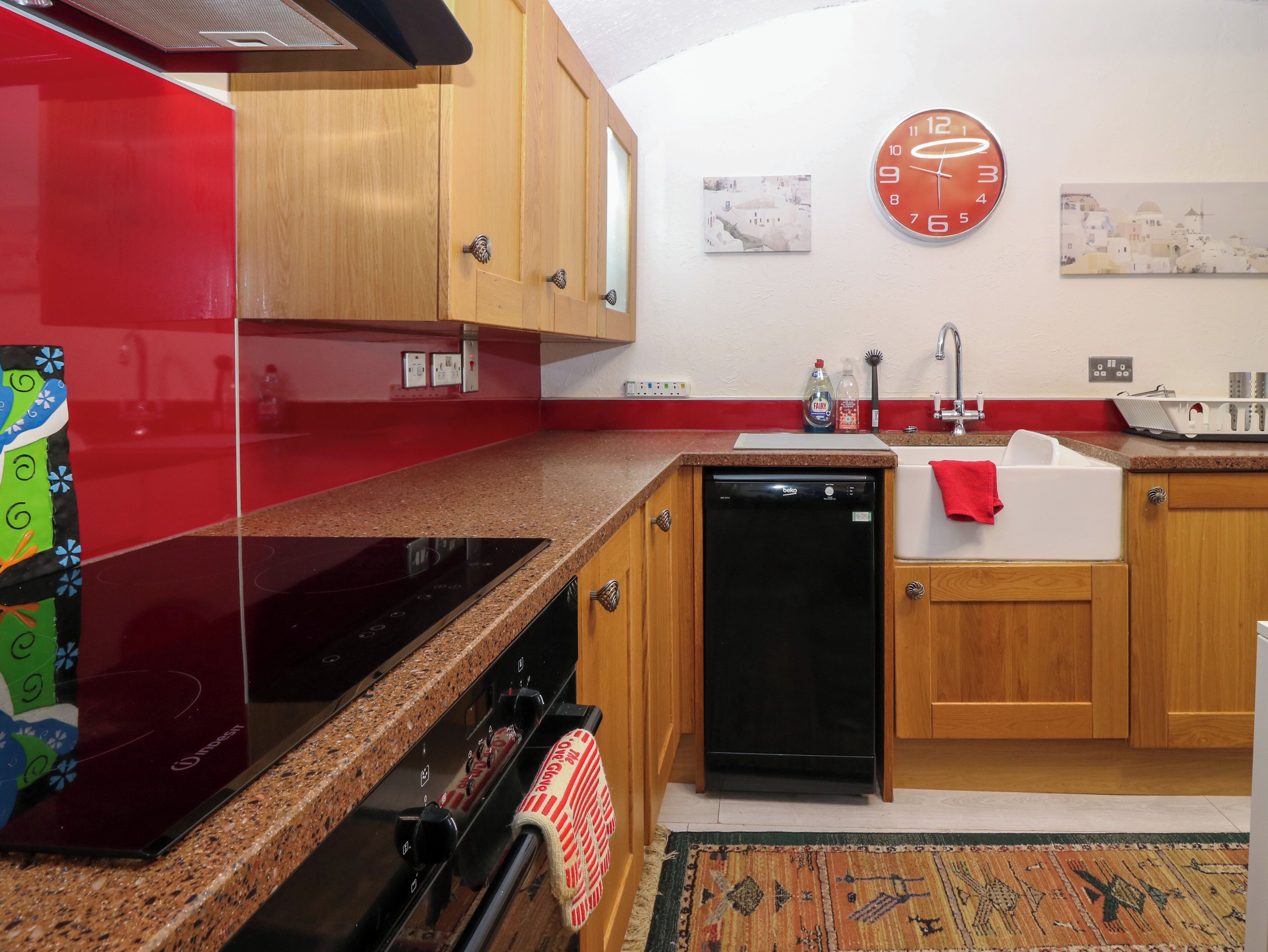 A kitchen with wooden cabinets, a black dishwasher, a red refrigerator, and a clock on the wall.