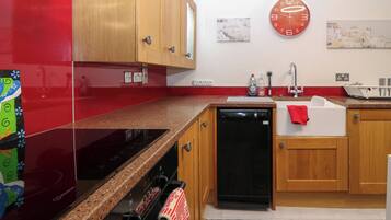Una cocina con armarios de madera, lavavajillas negro, refrigerador rojo y un reloj en la pared.