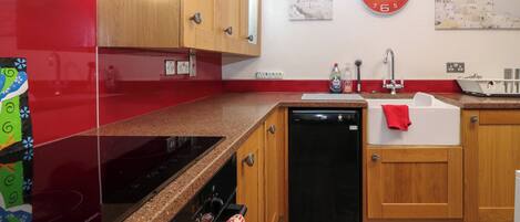 A kitchen with wooden cabinets, a black dishwasher, a red refrigerator, and a clock on the wall.