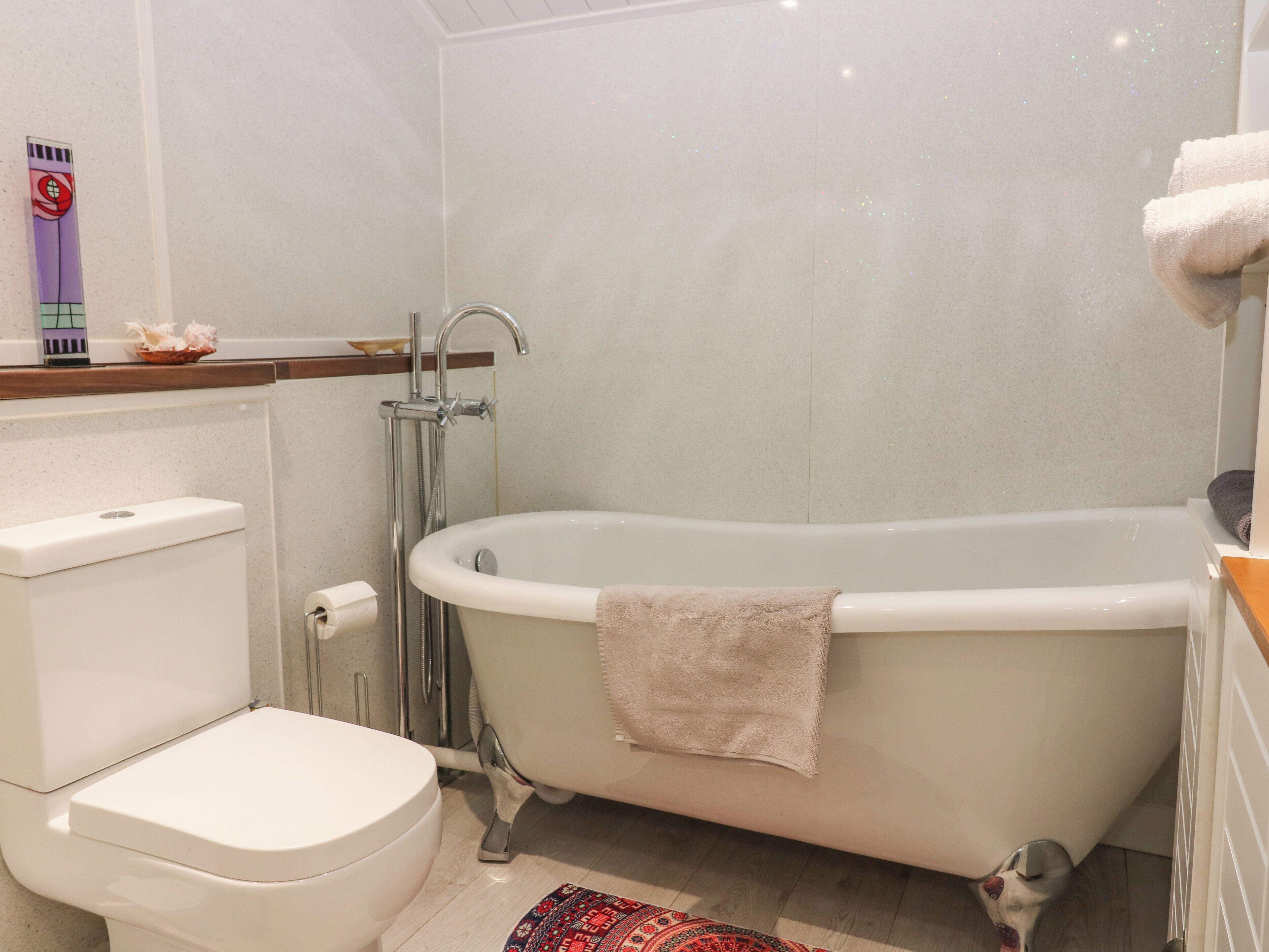 Un baño con inodoro blanco, bañera independiente con toalla y cabezal de ducha.