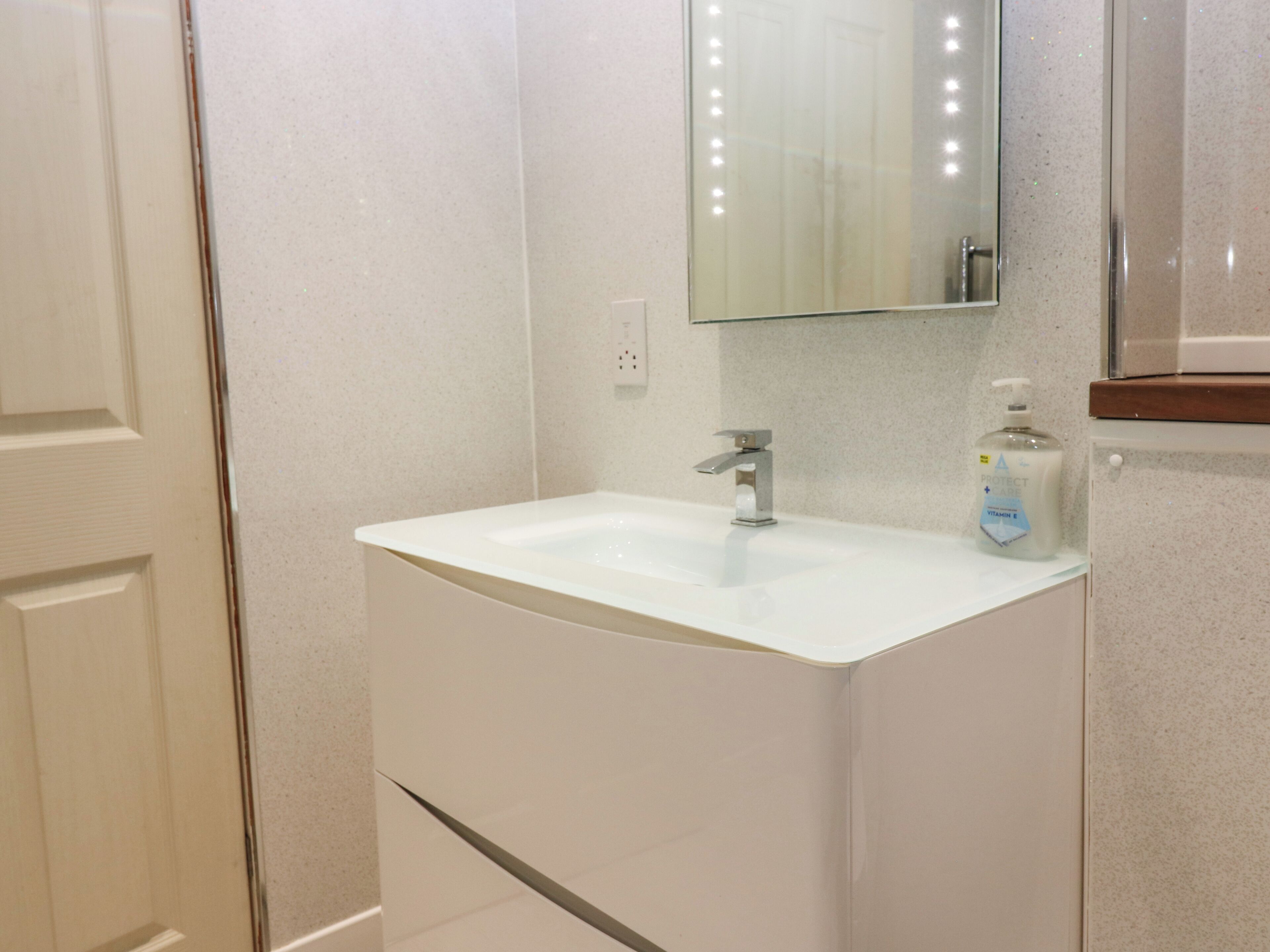 A bathroom with a white sink, a mirror, and a bottle of hand soap.