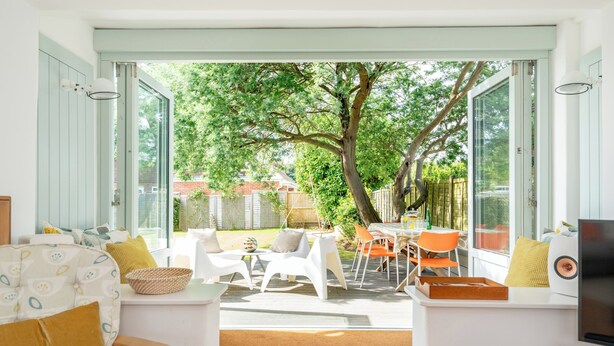 Een open leefruimte met uitzicht op een tuin, met een bank, stoelen, een tafel en een televisie.