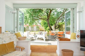 Un espace de vie à aire ouverte donnant sur un jardin, comprenant un canapé, des fauteuils, une table et un téléviseur.