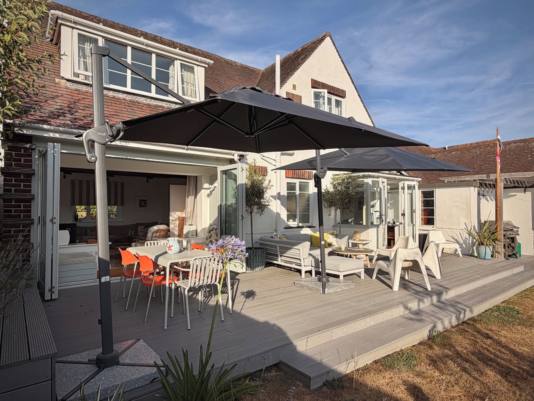 Un patio techado al aire libre con mesa y sillas, una parrilla y un gran paraguas.