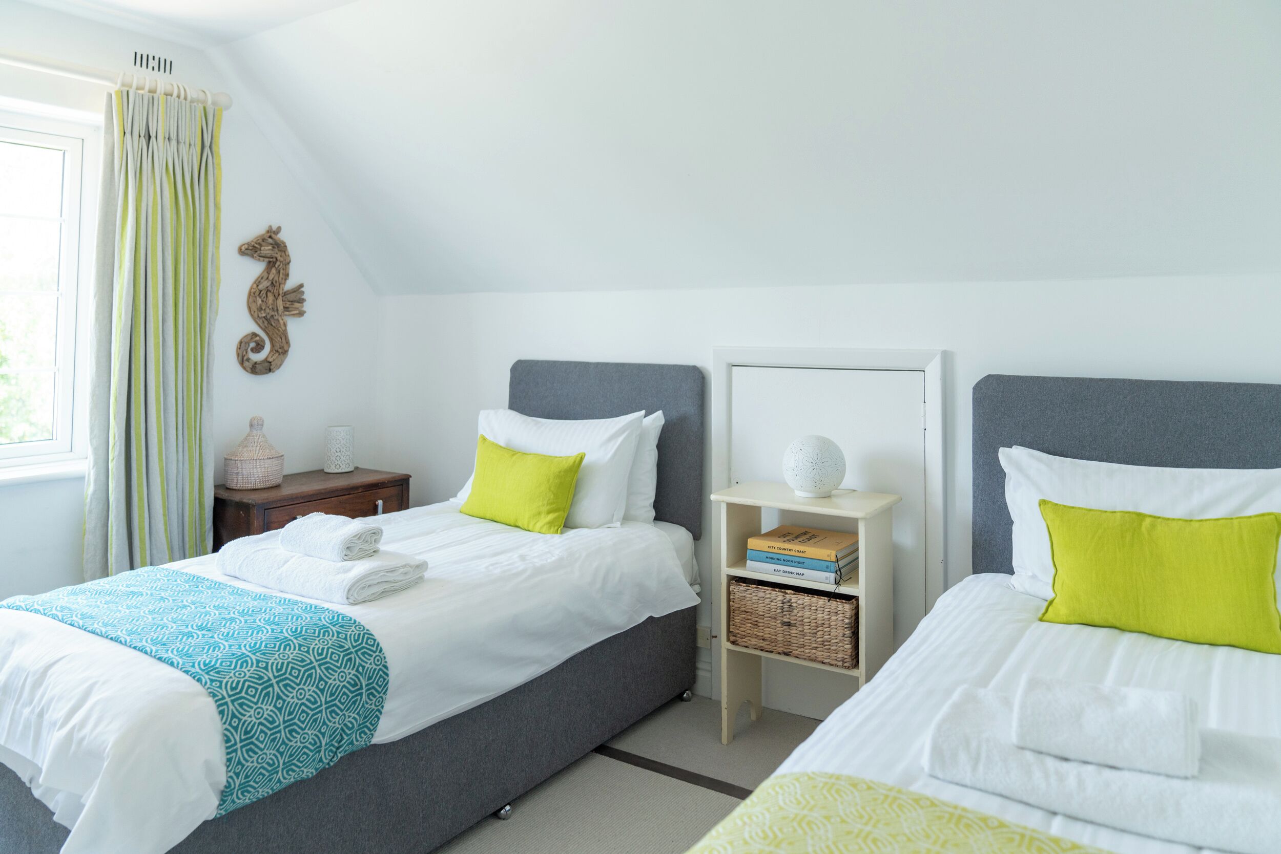 A bedroom with two beds, a bedside table with a lamp, a bookshelf, and a decorative seahorse.