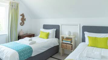A bedroom with two beds, a bedside table with a lamp, a bookshelf, and a decorative seahorse.