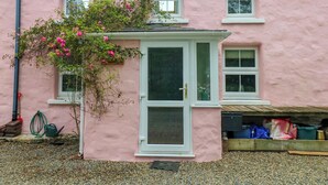 A pink house with a white door and windows, a garden with pebbles, and a wooden structure under the house. - 2 Summerhill (Haverfordwest)