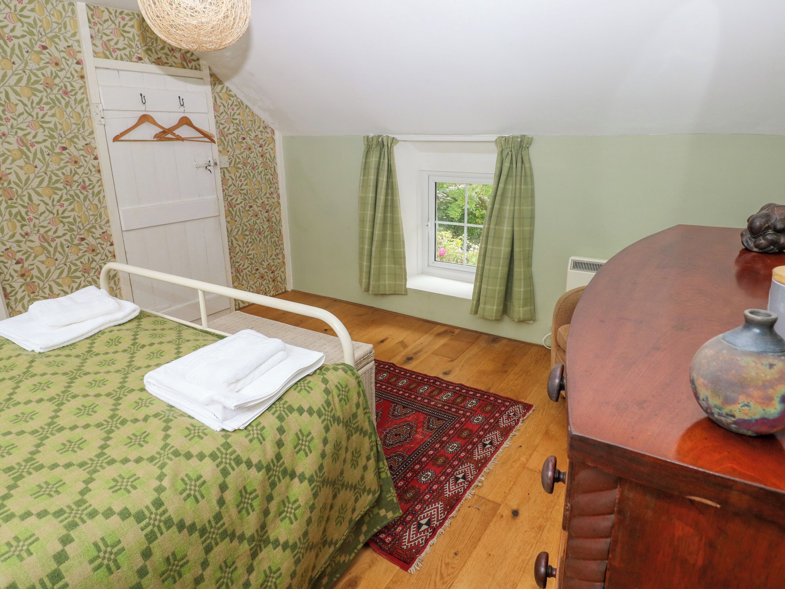 A bedroom with a single bed, a wooden dresser, a window with curtains, and a hanging light fixture.