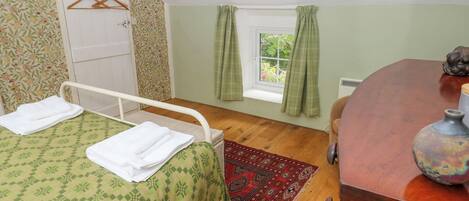 A bedroom with a single bed, a wooden dresser, a window with curtains, and a hanging light fixture.