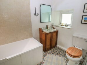 Une salle de bain avec une baignoire, un meuble en bois, un lavabo, un miroir, des toilettes et des carreaux de sol à motifs.