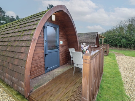 A wooden pod-style accommodation with a door, a small porch, and a chair.