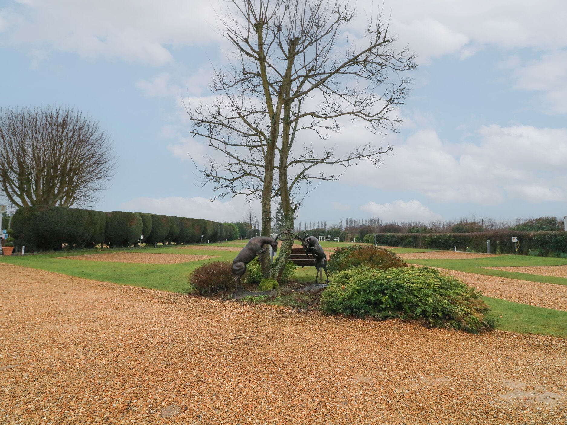 A landscaped area with a trimmed hedge, a gravel path, and a statue of a figure with a horse.