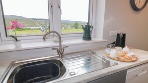 Una cocina con un lavamanos, una ventana que ofrece vistas al campo, un reloj en la pared y una cafetera sobre la encimera.