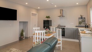 Una cocina moderna con armarios blancos, una campana extractora de acero inoxidable y un comedor con mesa y sillas blancas.