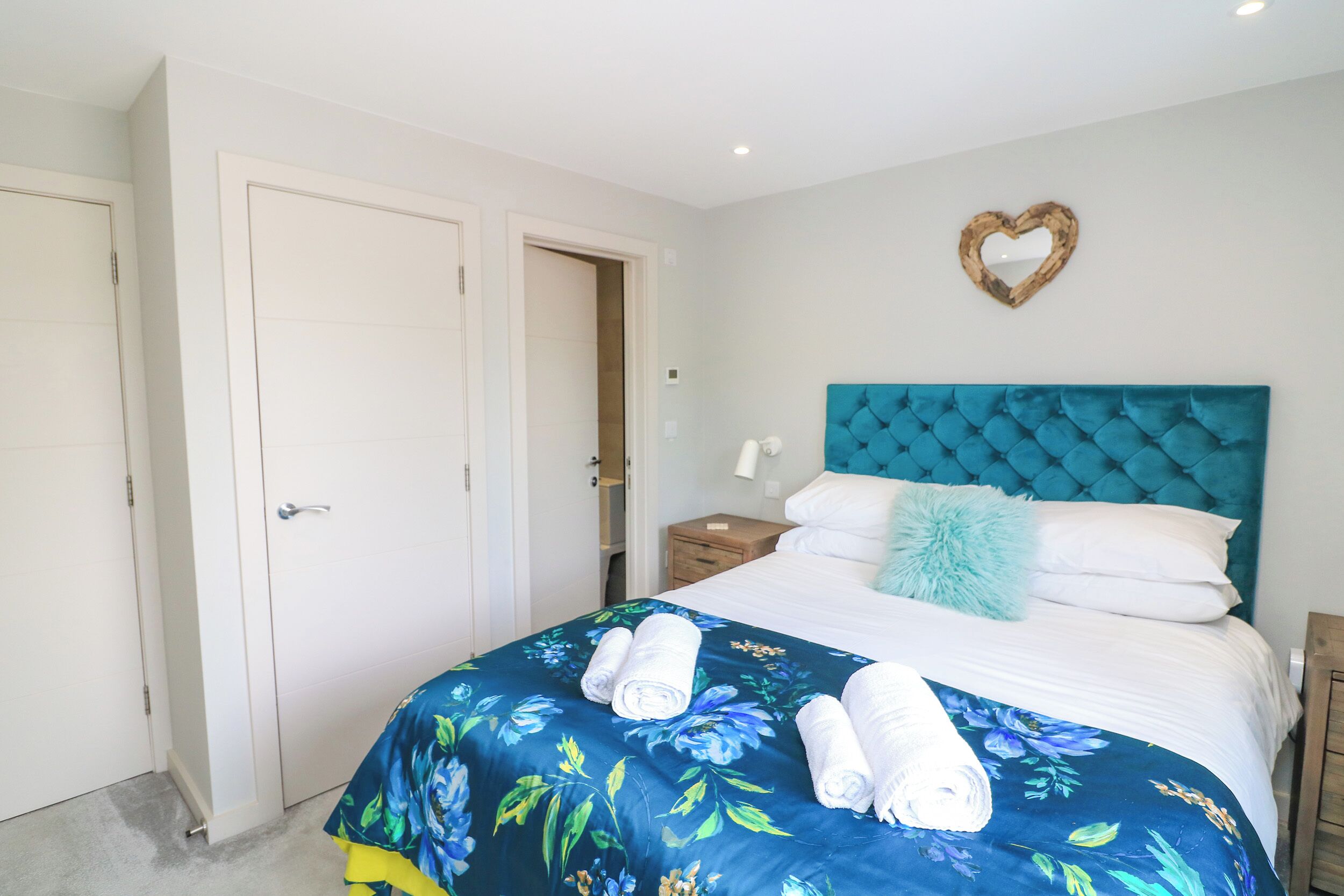 A bedroom with a large bed, a heart-shaped mirror on the wall, and a door to the left.