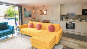 A modern living room with a yellow sofa, teal armchair, and a dining area with a table and chairs. - 2 De Courcey House (Dartmouth)