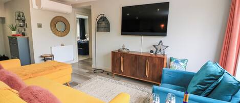 A modern living room with a flat-screen TV, a wooden cabinet, and a blue sofa.