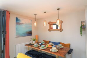 A dining area with a wooden table, multiple chairs, hanging pendant lights, and a large abstract painting on the wall.