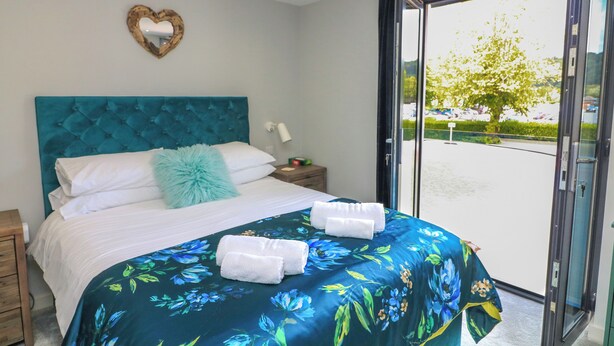 A bedroom with a large bed, a heart-shaped mirror, and a view of a parking lot through a glass door. - 2 De Courcey House (Dartmouth)