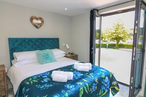 A bedroom with a large bed, a heart-shaped mirror, and a view of a parking lot through a glass door. - 2 De Courcey House (Dartmouth)