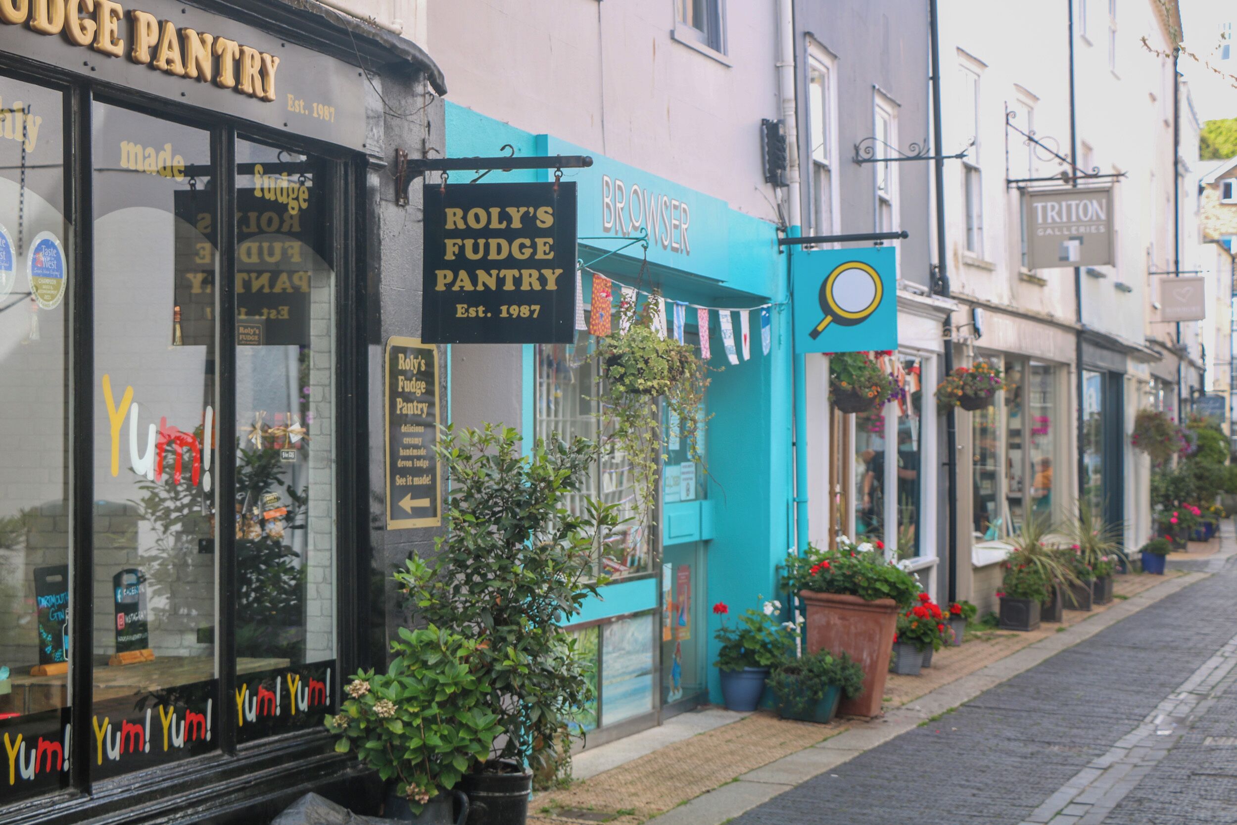 A street with storefronts, including a bakery named 'Roly's Fudge Pantry' and a gallery named 'TRITON GALLERIES'.