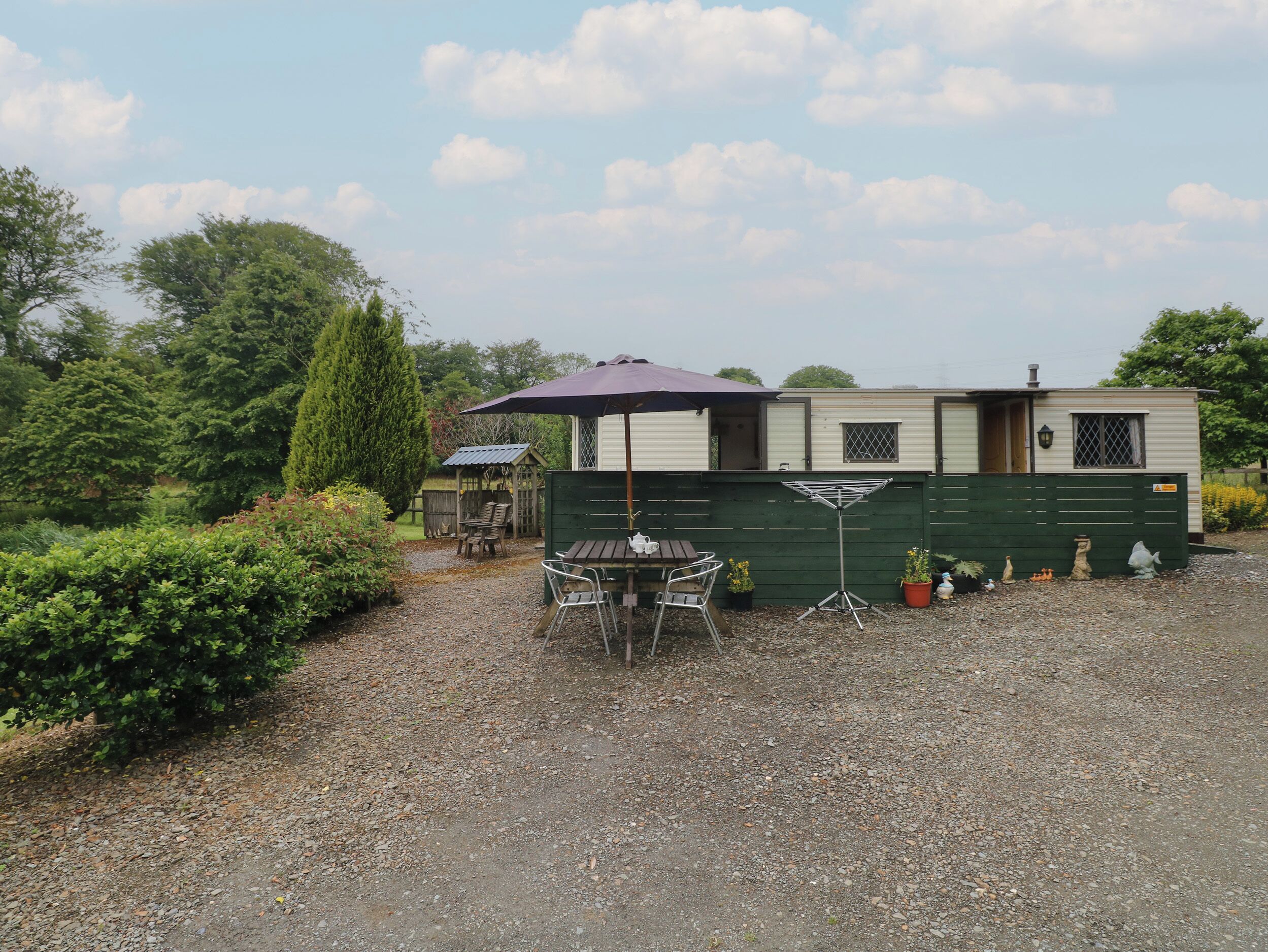 A mobile home with a patio area, including a table and chairs, a drying rack, and potted plants.