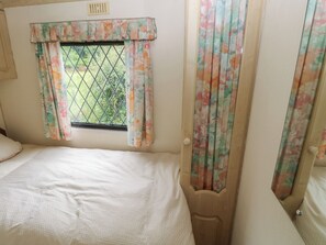 A bedroom with a bed, a window with floral curtains, and a door with a similar curtain design. - Lazy Trout Caravan (Narberth)