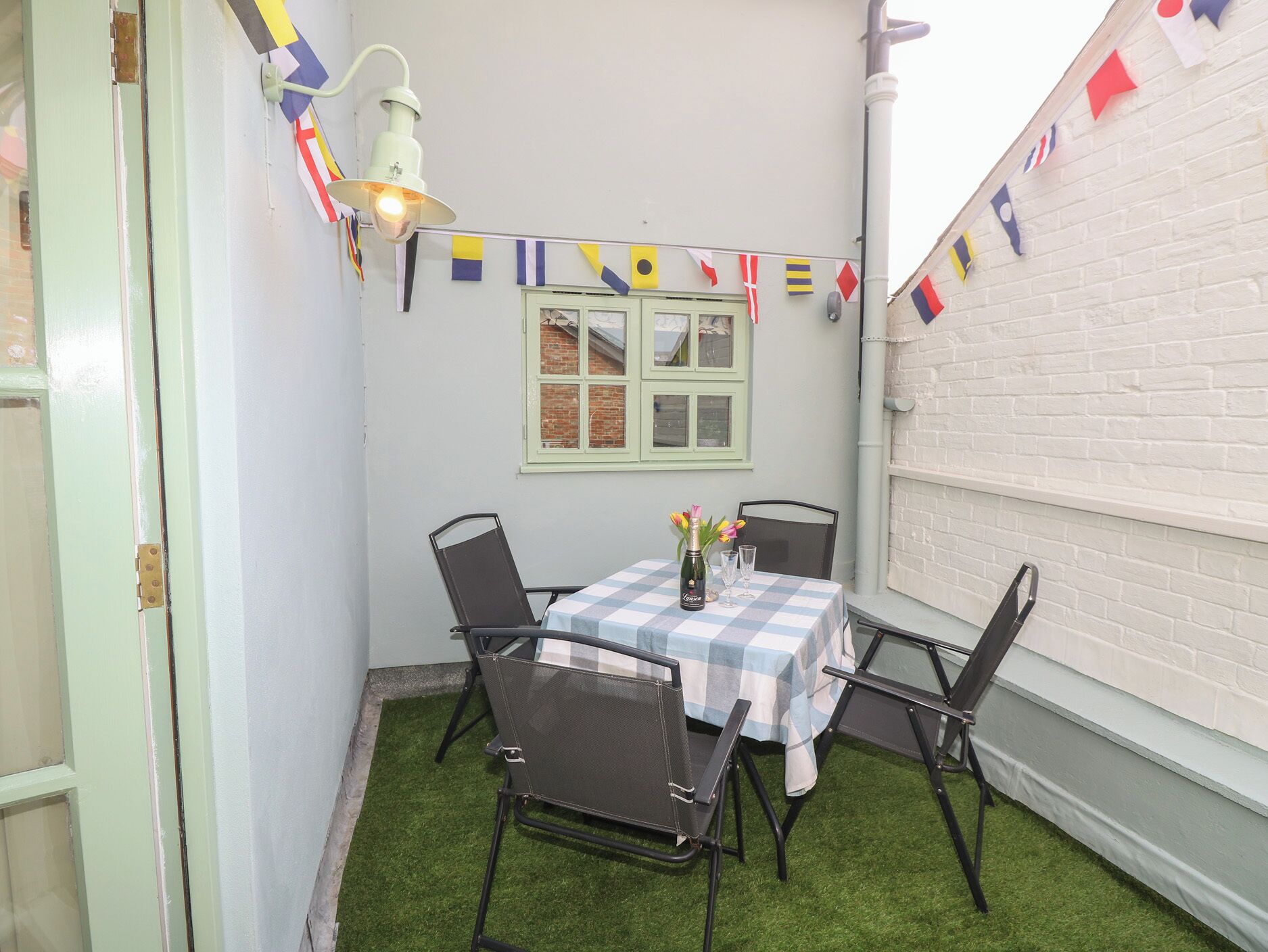 En lille terrasse med et bord og stole, en flaske champagne og en række farverige flag.