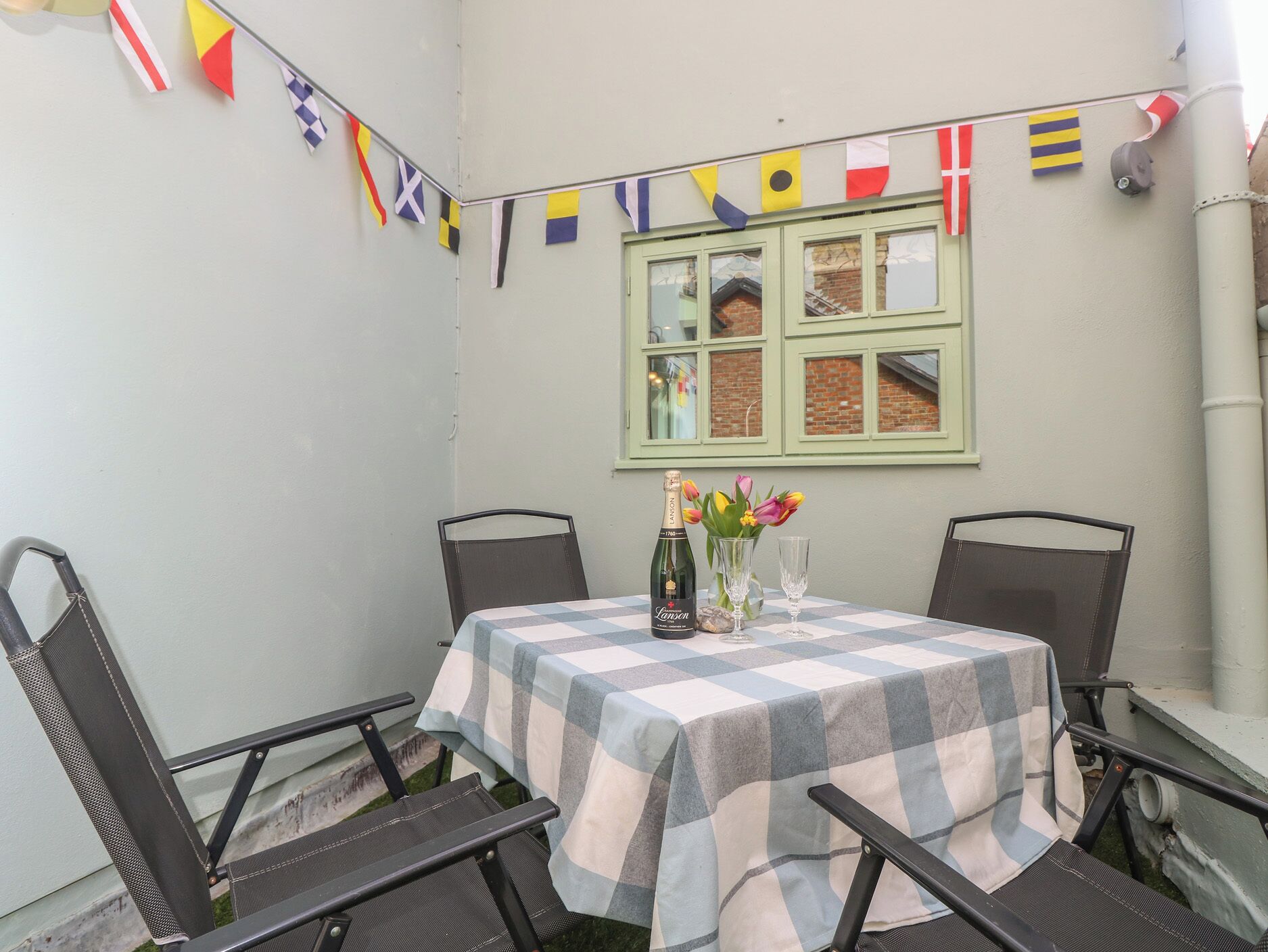 Una mesa dispuesta con mantel a cuadros, dos sillas, una botella de champán y un jarrón con flores.