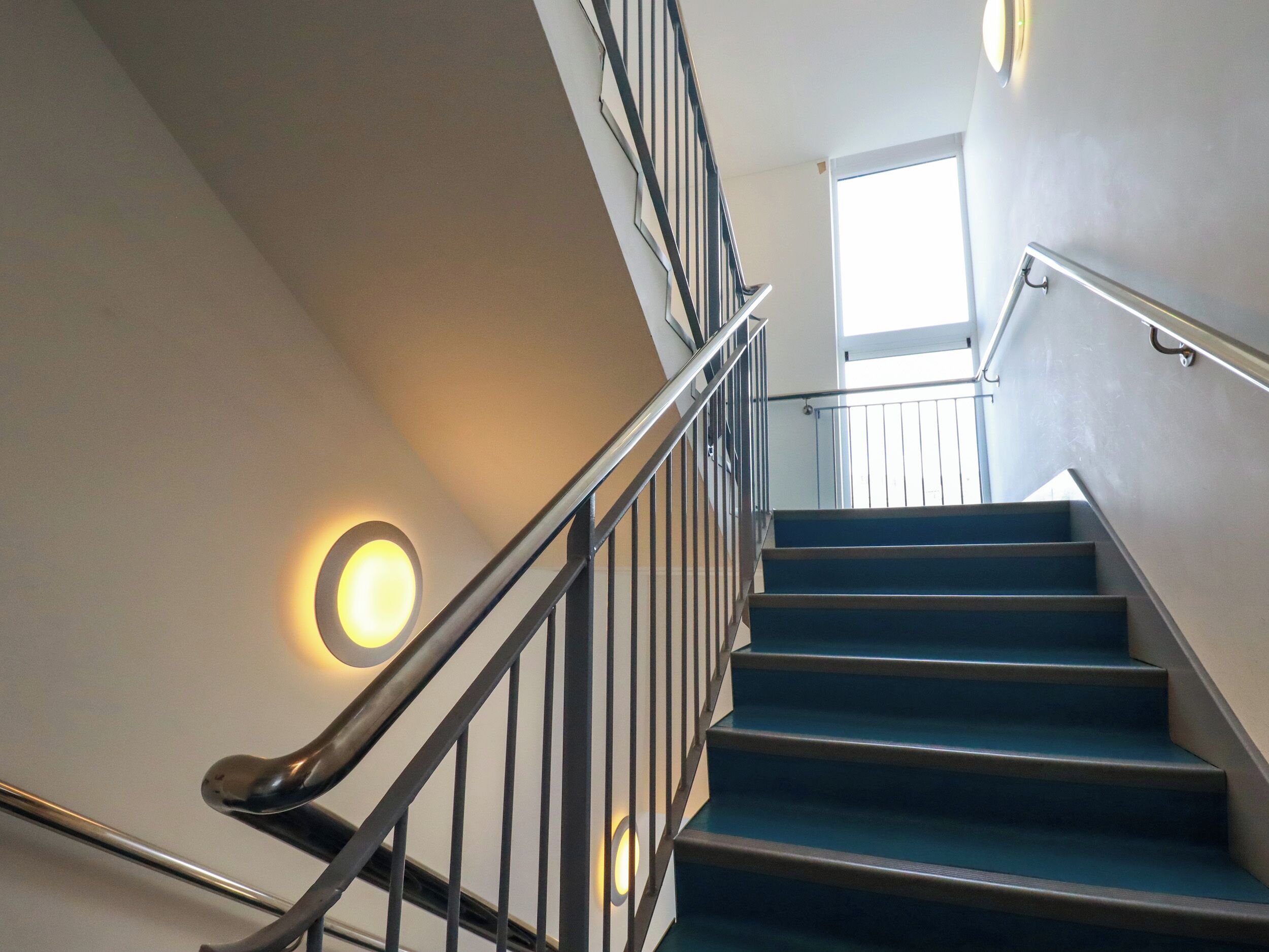 A staircase with a handrail and wall-mounted lights.