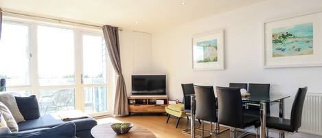 A modern living room with a sofa, a coffee table, a TV, and a dining area with chairs and a table.
