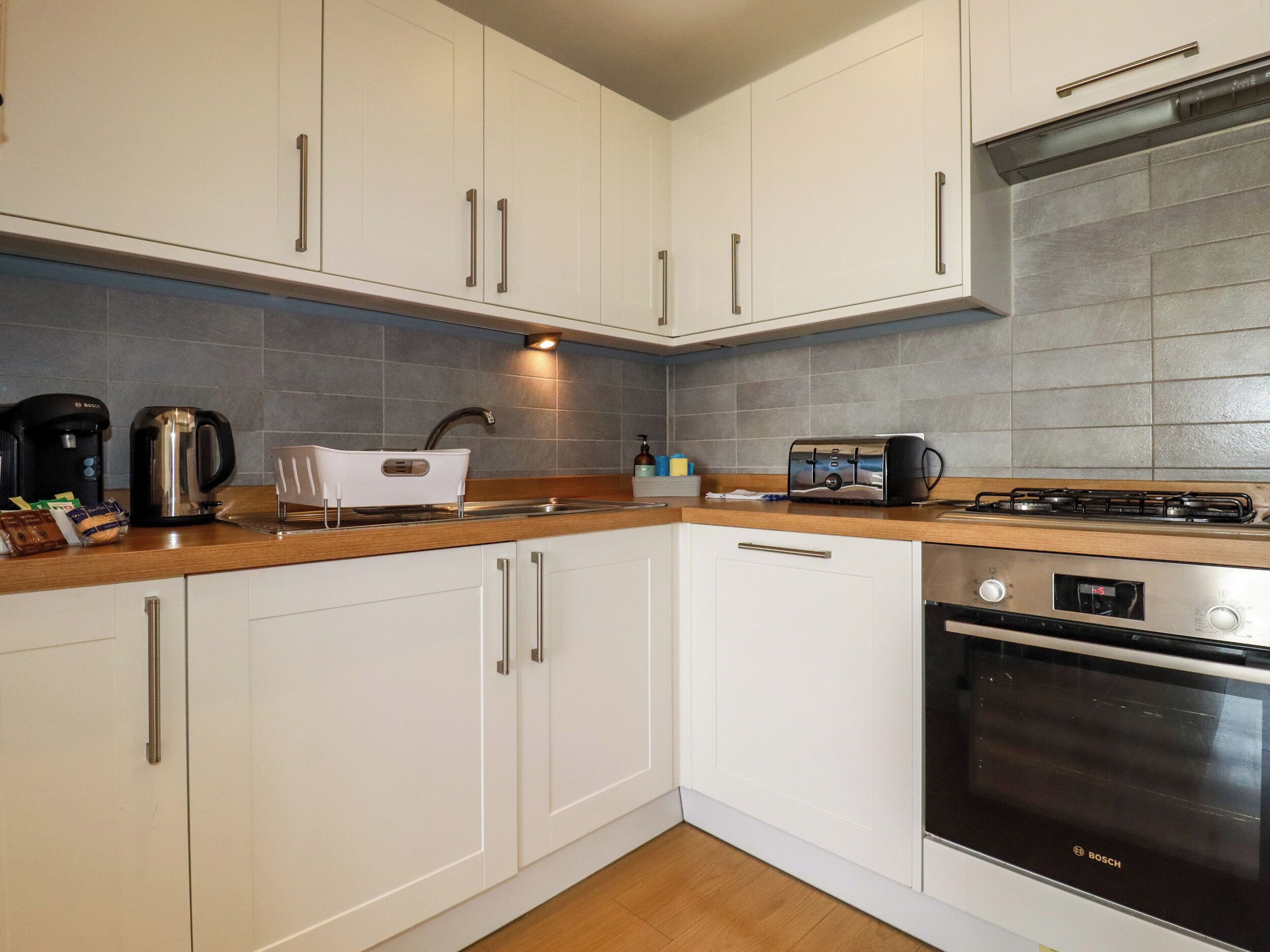 A modern kitchen with white cabinets, a Bosch oven, a toaster, and a kettle.