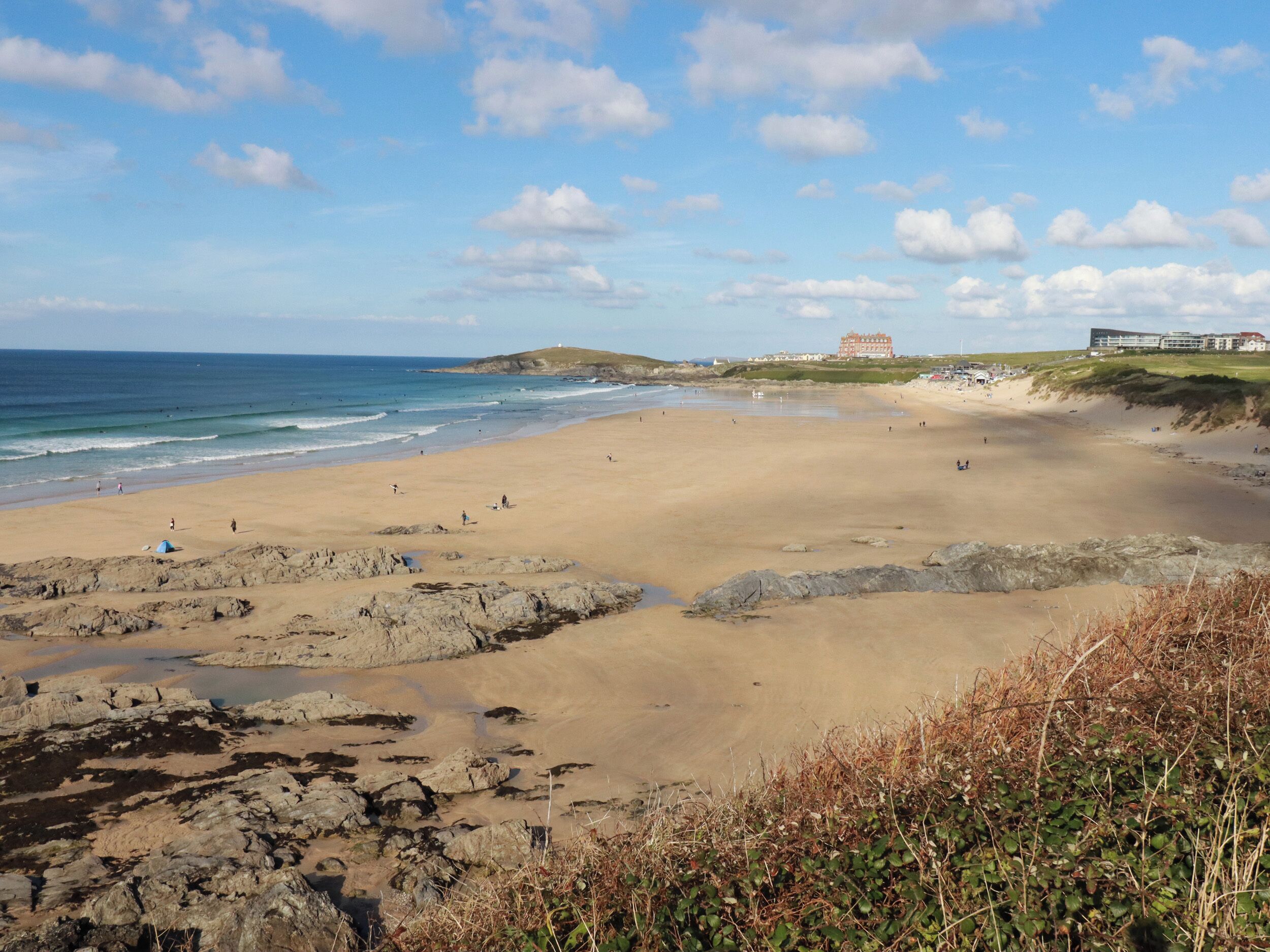 A beach with rocky areas, a large building in the background, and the ocean.