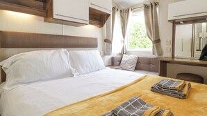 Un letto rifatto con lenzuola bianche e una coperta gialla, una testiera in legno, un comodino con uno specchio e una finestra con tende.