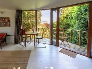 A room with a sliding glass door leading to a balcony with a view of greenery and a distant landscape. - The Bothy (Lyme Regis)