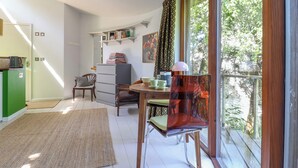 A cozy room with a dining table, chairs, a kitchen area, and a large window with a view of trees. - The Bothy (Lyme Regis)