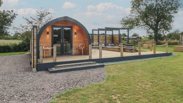 A small, wooden structure with a curved roof, a glass door, and a seating area with chairs. - Paradise (Market Drayton)